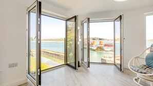 Habitació amb una gran porta corredissa de vidre que dona a una vista d'aigua i edificis industrials.