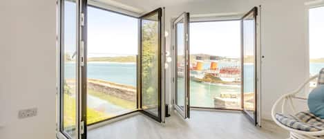 A room with a large sliding glass door leading to a view of a body of water and industrial structures.