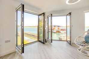 A room with a large sliding glass door leading to a view of a body of water and industrial structures. - 1 Bed in Padstow (oc-t32456) (Padstow)