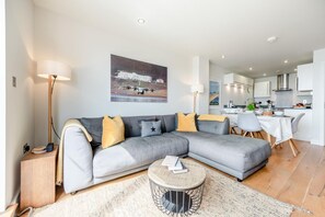 Un salon moderne avec un canapé d’angle gris, une table basse ronde et une cuisine en arrière-plan.