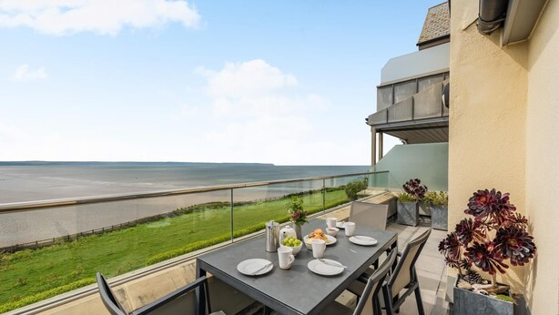A balcony with a table set for two, overlooking a beach and ocean. - 2 Bed in Saunton (oc-10ocea) (Croyde)