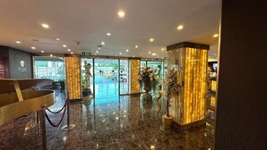 Eine Hotelhalle mit Marmorboden, einer Rezeption und einem Glasgang nach draußen.