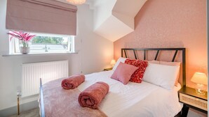 Et soveværelse med seng, sengeborde, lampe og radiator samt et vindue med udsigt.