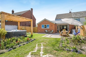 Ein Garten mit Whirlpool, einer Holzpergola und einem Ziegelhaus mit Terrasse.