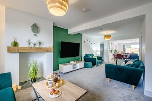 Ein modernes Wohnzimmer mit einem Flachbildfernseher, türkisfarbenen Sofas, einem Couchtisch mit Gebäck und einer grünen Akzentwand.