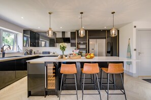 Une cuisine moderne dotée d’un îlot central, de tabourets de bar, de luminaires suspendus et offrant une vue sur l’extérieur.