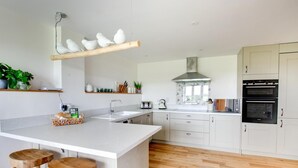 A modern kitchen with a central island, wooden stools, a built-in oven, and a hanging light fixture with white bird sculptures. - 2 Bed in Newton (oc-swro) (Newton)