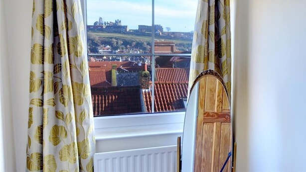 Ein Zimmer mit großem Fenster und Blick auf eine historische Stadtlandschaft mit roten Dächern und einer Burg.