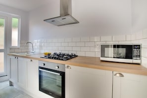 A modern kitchen with white cabinets, a gas stove, an oven, a microwave, and a window. - 2 Bed in Southwold (oc-4east) (Southwold)