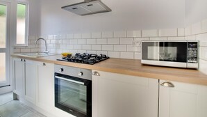 Una cucina moderna con mobili bianchi, un piano di lavoro in legno, un fornello a gas, un forno e un microonde.