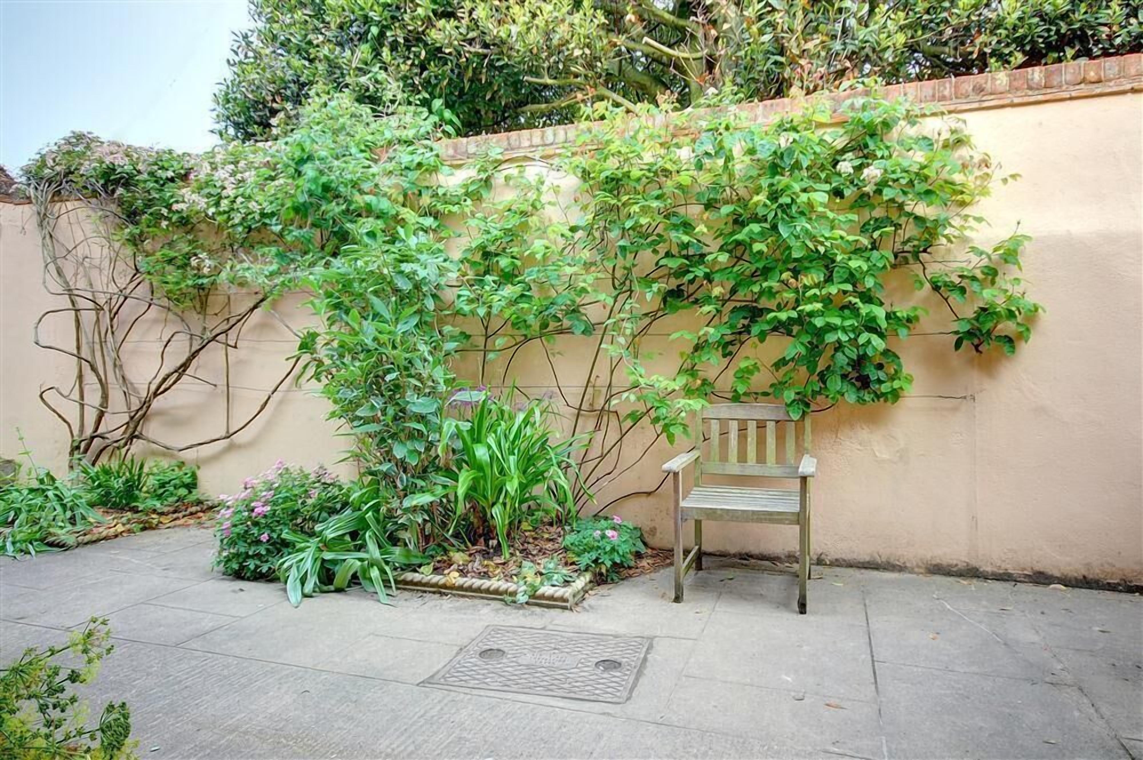 Eine Bank in einem Garten mit Mauerwerk und unterschiedlichen Pflanzen.