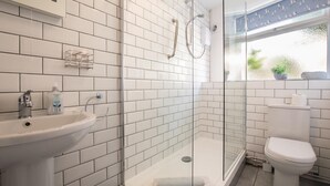 Un bagno moderno con piastrelle bianche, cabina doccia in vetro, lavabo e WC.