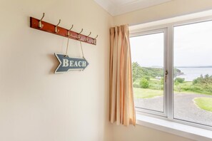 A room with a window overlooking a landscape, a coat rack with hooks, and a directional sign pointing to the beach.