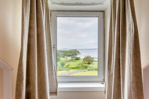 A window with curtains, offering a view of a landscape with greenery and a body of water.