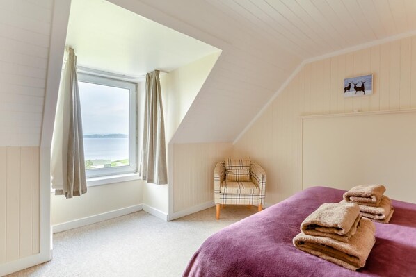 A bedroom with a bed, a chair, a window with curtains, and a view of the sea.