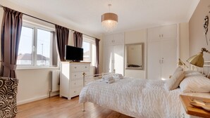 A bedroom with a bed, dresser, TV, and a large mirror. - 3 Bed in Whitby (oc-w015) (Whitby)