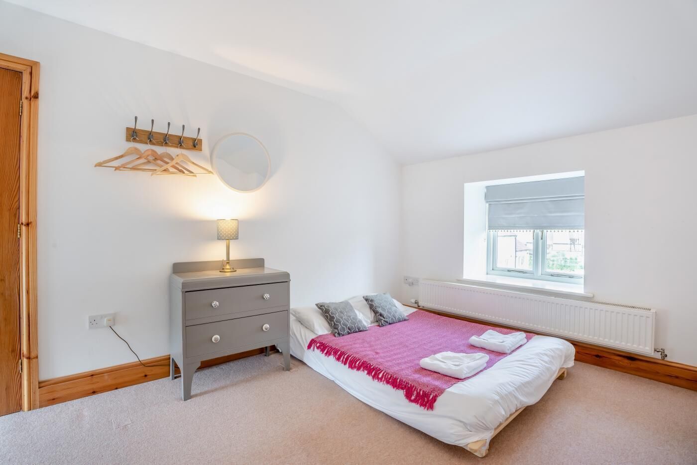 Une chambre à coucher avec un lit, une table de chevet avec une lampe, une fenêtre et un porte-manteau.