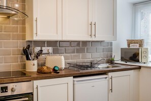 Una cucina con mobili bianchi, un tostapane, un forno a microonde e un cesto di vimini con un cartello che dice 'Benvenuti'.