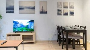A modern living room with a flat-screen TV, a dining table with chairs, and a wall decorated with landscape paintings. - AR IFEMA modern apartment near airport and trade fair Madrid (Madrid)