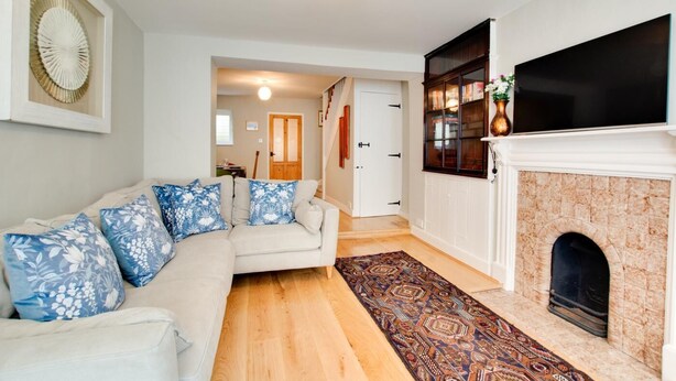 Una sala de estar con un sofá color beige, cojines estampados, una chimenea y un televisor de pantalla plana.