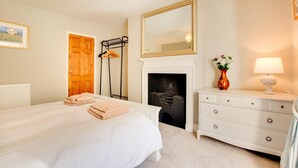 Un dormitorio con una cama grande, un aparador, un espejo, una chimenea y un perchero.