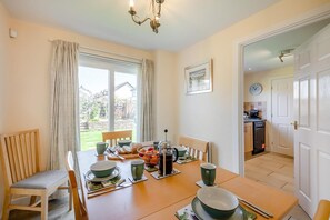 Un coin repas avec une table dressée pour quatre personnes, un banc et une vue sur le jardin.