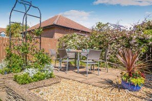 Une terrasse avec une table et des chaises, entourée de plantes et d’une clôture en bois.