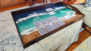 A wooden tray table with a sea-themed design, a patterned bedspread, and a wooden dresser in the background.