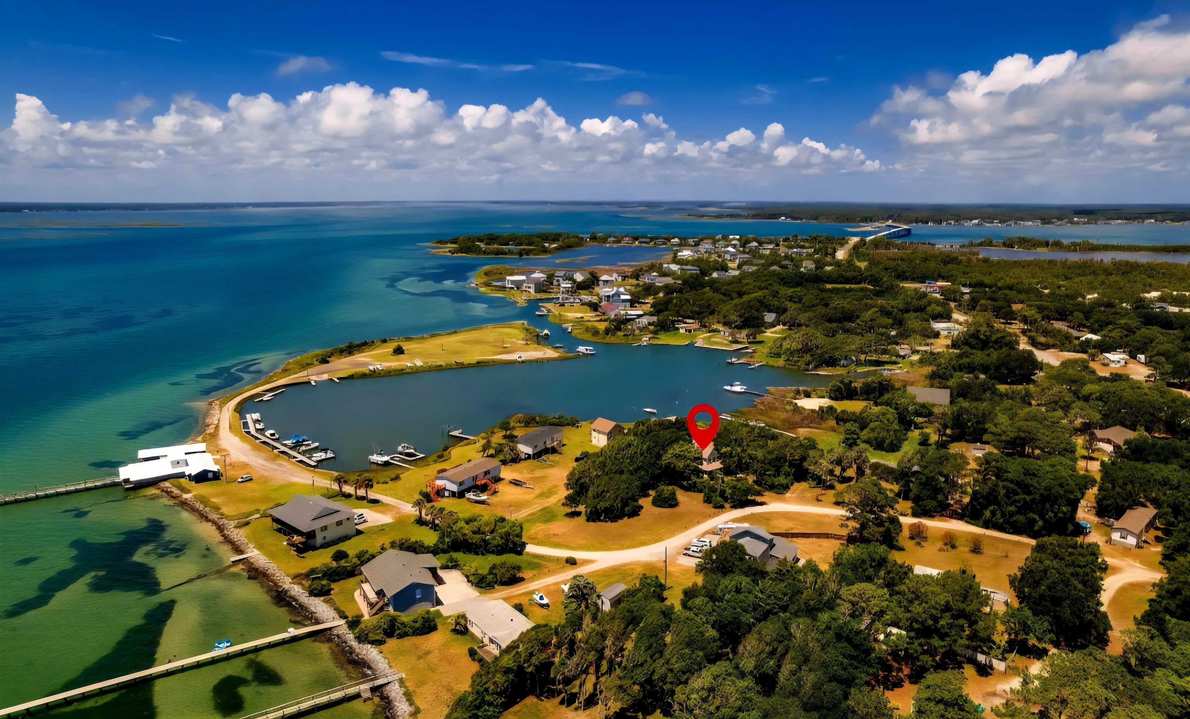 An aerial view of a coastal residential area with clear blue waters, a marina, and houses surrounded by greenery.