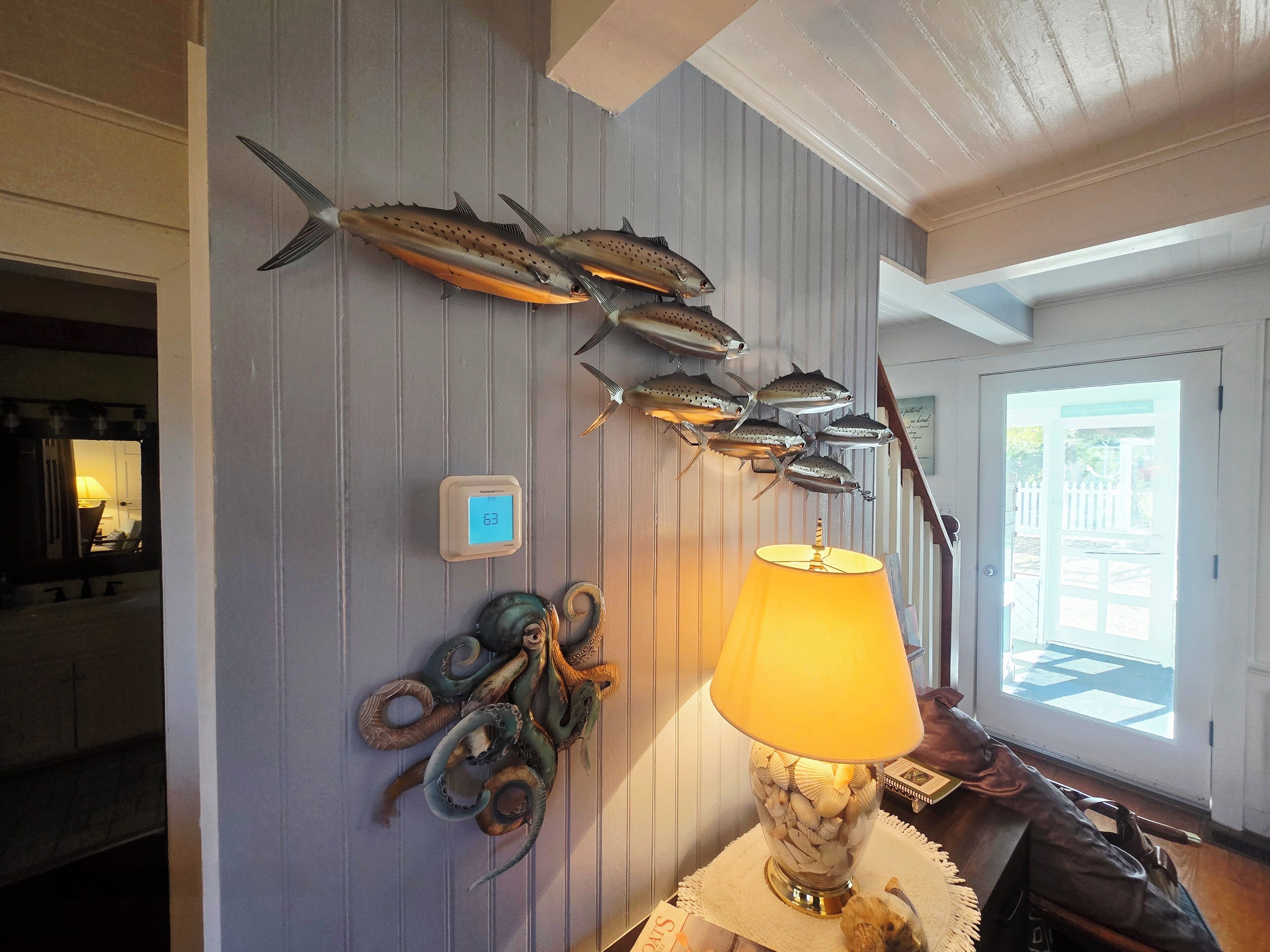A room with a wall-mounted fish decoration, a thermostat, and a lamp with a shell base.