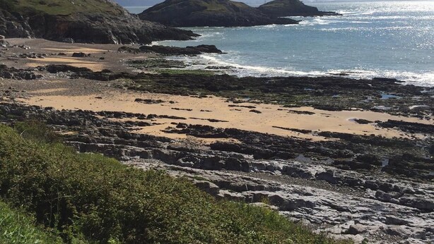 A coastal landscape with rocky terrain, a sandy beach, and a lighthouse on a small island.
