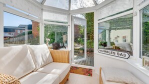 A conservatory with a white sofa, wicker furniture, and a view of a garden.