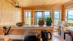 Ein Holzblockhaus mit Küchenzeile, einem Esstisch und Blick ins Freie.