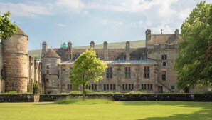 Ein historisches Steinhaus mit mehreren Schornsteinen und einer großen Rasenfläche davor.