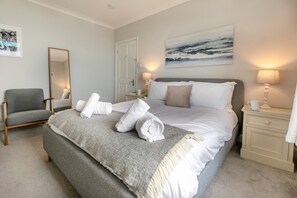 Een keurig opgemaakt slaapkamer met een bed, een stoel, een nachtkastje en een spiegel aan de muur.