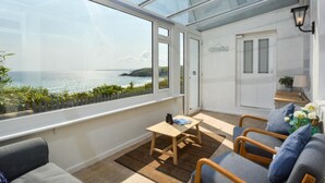 Um quarto iluminado pelo sol com vista para o mar, uma mesa de madeira e um sofá.