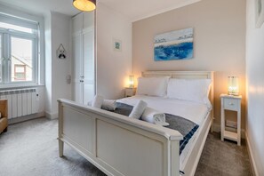 A bedroom with a bed, bedside tables, a radiator, a window, and a painting on the wall. - 3 Bed in Praa Sands (oc-p00859) (Praa Sands)