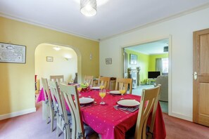 A dining room with a table set for four, chairs, a fruit bowl, and a television in the background. - 4 Bed in Ilkley (oc-ds168) (Ilkley)