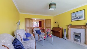 A living room with a fireplace, a dining area, and a hallway leading to another room. - 4 Bed in Ilkley (oc-ds168) (Ilkley)
