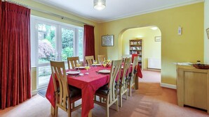 A dining room with a red tablecloth, wooden chairs, and a view of the outdoors through large windows. - 4 Bed in Ilkley (oc-ds168) (Ilkley)