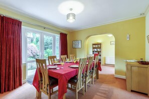 A dining room with a red tablecloth, wooden chairs, and a view of the outdoors through large windows. - 4 Bed in Ilkley (oc-ds168) (Ilkley)