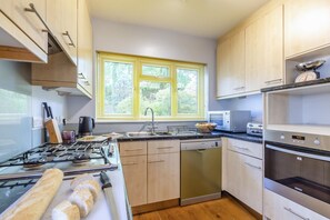 Une cuisine moderne équipée d’une cuisinière à gaz, d’un lave-vaisselle, d’un four et d’une fenêtre avec des stores.