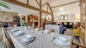 A spacious dining area with a long table set for a meal, a kitchen in the background, and a living area with a sofa and chairs. - 4 Bed in Cawton (oc-t32408) (Cawton)
