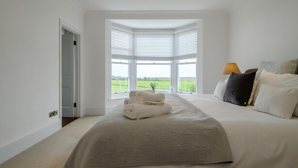 A bedroom with a large bed, a view of a green field through a bay window, and a lamp on the nightstand. - 5 Bed in Southwold (oc-tomill) (Southwold)