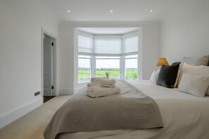 A bedroom with a large bed, a view of a green field through a bay window, and a lamp on the nightstand. - 5 Bed in Southwold (oc-tomill) (Southwold)