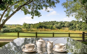 A glass table with tea set and a view of a golf course.