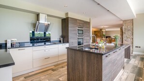 A modern kitchen with a large island, built-in oven, and a stone accent wall. - 4 Bed in Catsash (oc-u32332) (Newport)