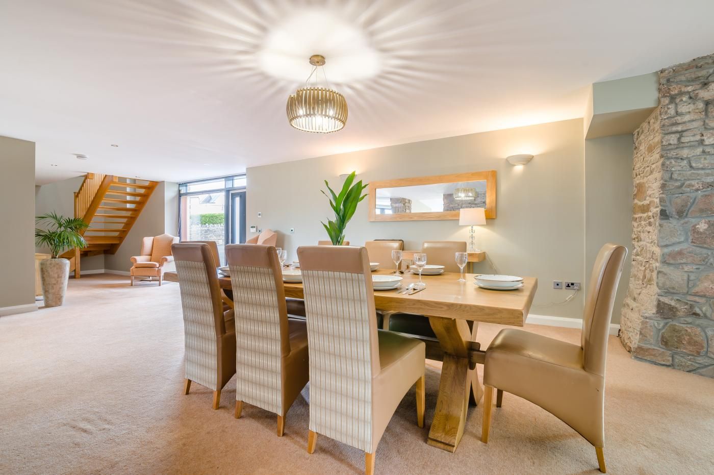 Un espace repas comprenant une table en bois, des chaises recouvertes d’un tissu beige et un luminaire suspendu.