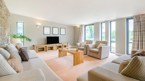 A spacious living room with a sofa set, a coffee table, a TV, and large windows. - 4 Bed in Catsash (oc-u32332) (Newport)