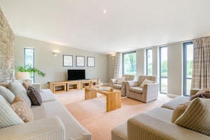 A spacious living room with a sofa set, a coffee table, a TV, and large windows.